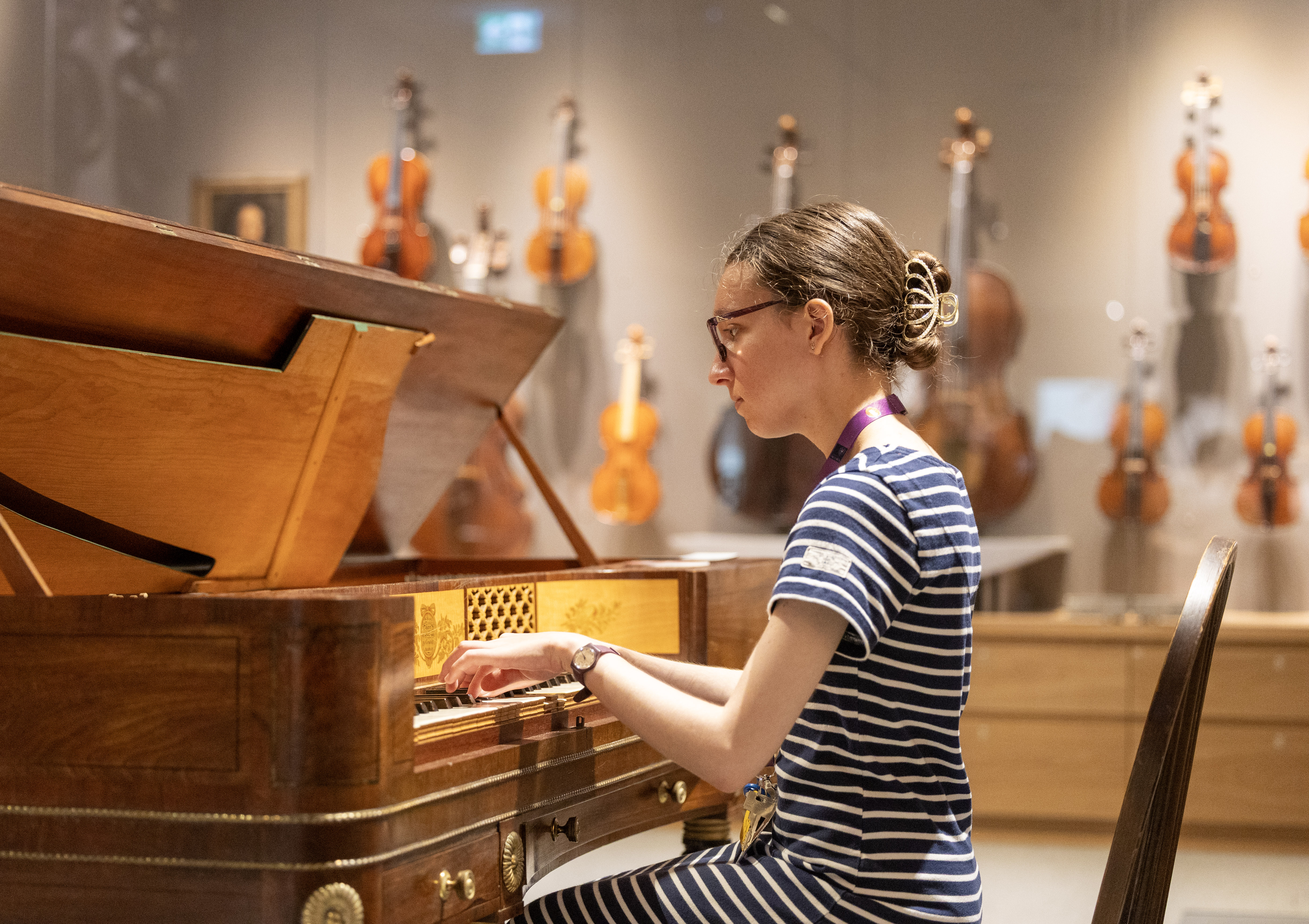 student at piano, violins displayed behind